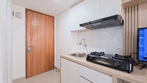 A compact kitchen with a stove, sink, and wooden door. - Good Location Studio Near Cisauk Station At Cisauk Point Apartment (Cisauk)