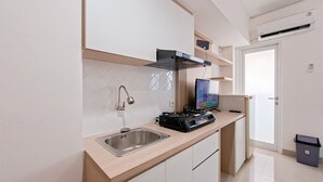 A modern kitchen with a stainless steel sink, a gas stove, and a television. - Good Location Studio Near Cisauk Station At Cisauk Point Apartment (Cisauk)