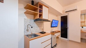 Una cucina compatta con lavello incassato, microonde e piccolo frigorifero. Sopra il lavello si trova un pensile in legno e una TV a schermo piatto montata a parete.