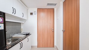 Ett kök med vita skåp, en svart bänkskiva, en trädörr och en liten ventilationsöppning.