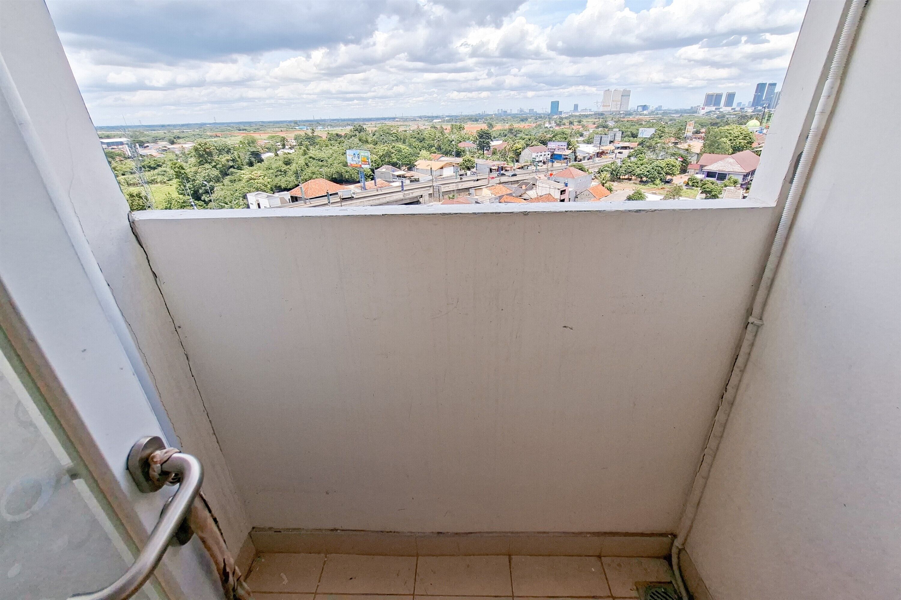 A room with a view of a cityscape, a door with a metal handle, and a tiled floor.