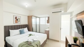 Une chambre d’hôtel avec un lit, un bureau équipé d’un ordinateur, un miroir et une fenêtre donnant sur la ville.