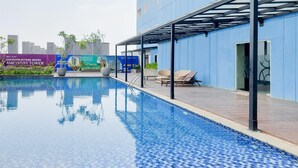 A swimming pool with tiled edges, a covered seating area, and a building with a blue exterior. - Homey And Minimalist Studio At Apartment Cisauk Point (Cisauk)