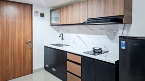 Moderni keittiö, jossa on marmoripintainen välitila, puukaapit, musta jääkaappi ja sisäänrakennettu mikroaaltouuni.