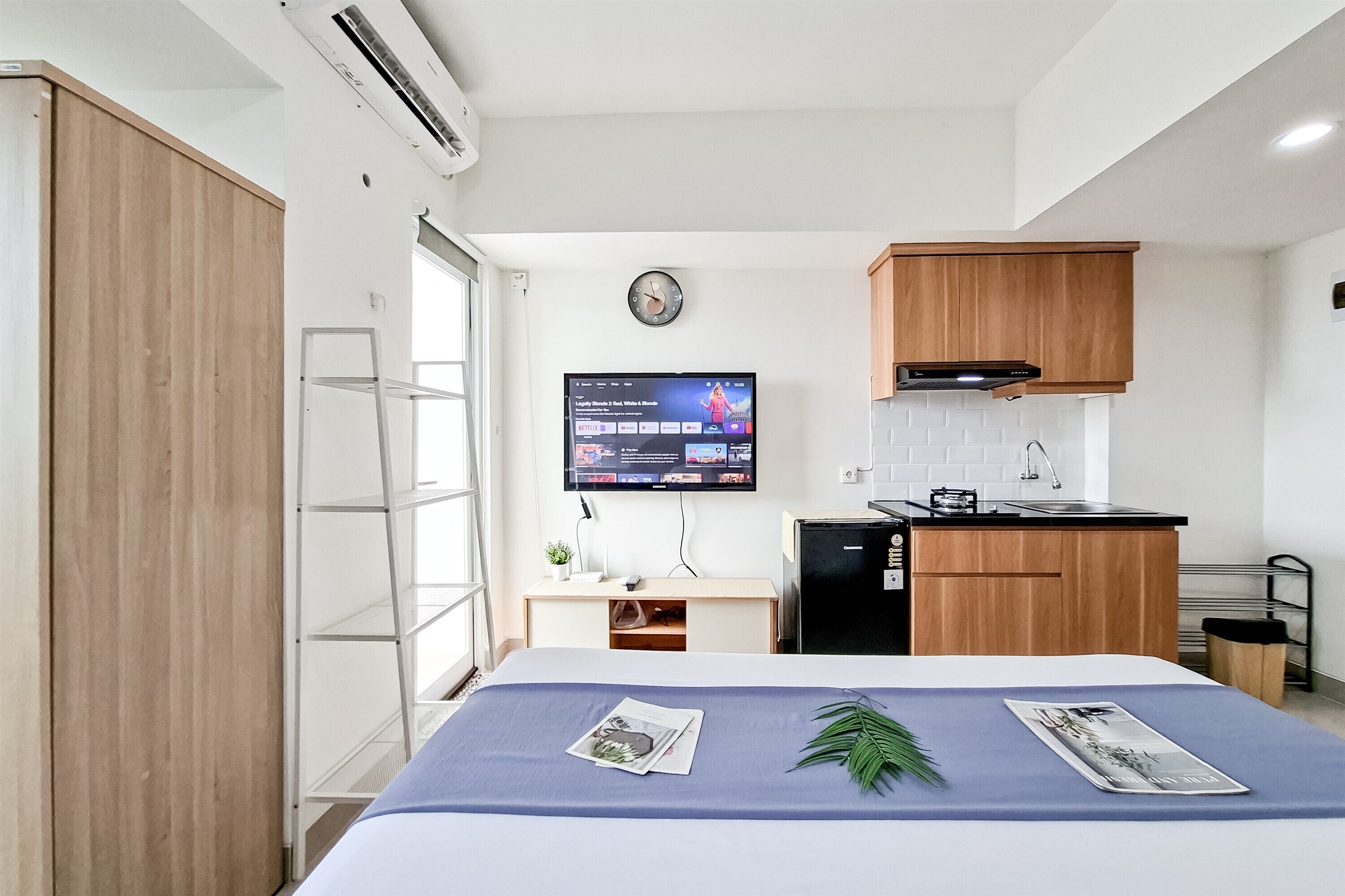Una habitación de hotel compacta con cama, televisión, kitchenette pequeño y armario de madera.