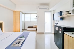 A modern hotel room with a bed, a desk, a refrigerator, and a television. - Good Location Studio At Cisauk Point Apartment (Cisauk)