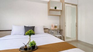 Een hotelkamer met een bed, nachtkastje, een kleine plant in pot, bedlampje, spiegel en een kledingkast.