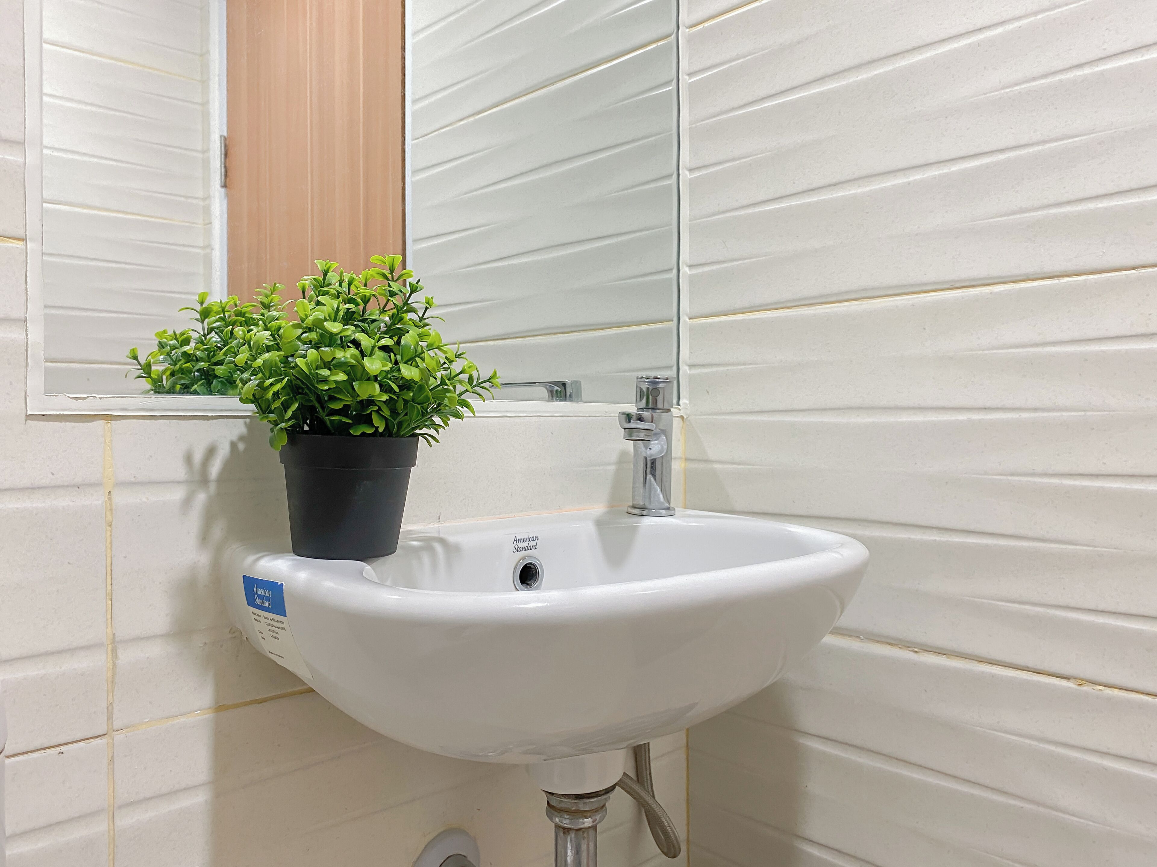 Un lavabo de salle de bain agrémenté d’une plante en pot, d’un miroir et d’un porte-serviettes fixé au mur.
