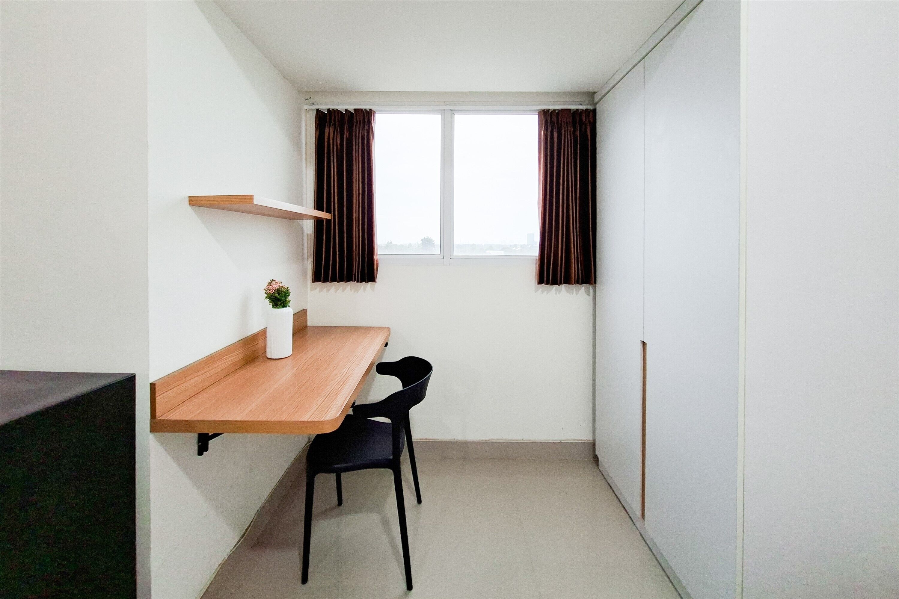 A small, narrow room with a wooden table and two chairs, a white shelf, and a window with curtains.