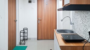 A compact kitchen with a wooden door, a black sink, a countertop with a black induction cooktop, and a speckled backsplash. - Serene Studio For 2 Pax At Cisauk Point Apartment (Cisauk)