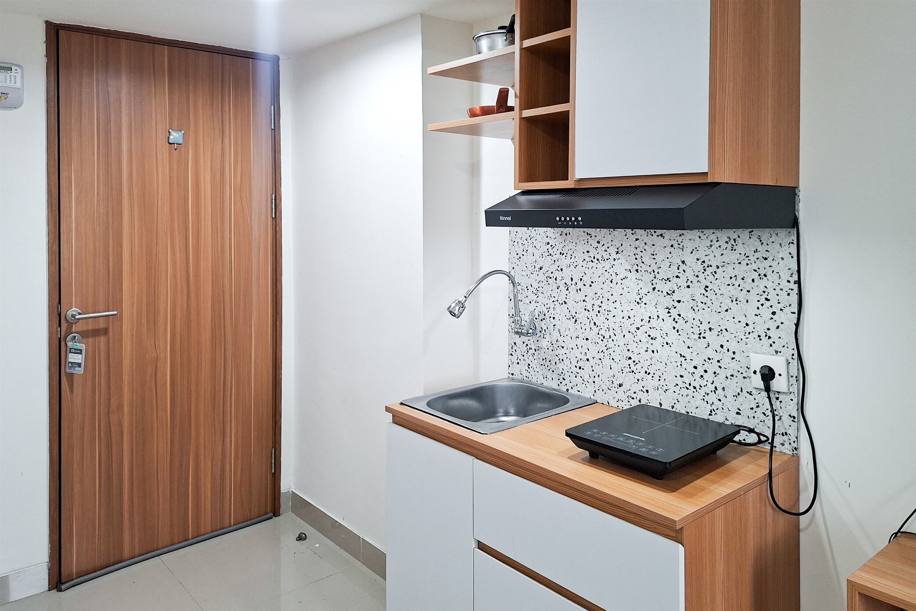 Een compacte keuken met een houten deur, witte kastjes, een roestvrijstalen spoelbak en een zwarte afzuigkap.