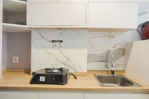A kitchen with a marble backsplash, a stainless steel sink, and a black portable stove. - Nice And Comfy Studio At Citra Living Apartment (Jakarta)