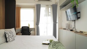 A hotel room with a bed, a desk, an air conditioning unit, a television, and a window with curtains. - Comfortable Space And Neat Studio At Apartment Citra Living (Jakarta)