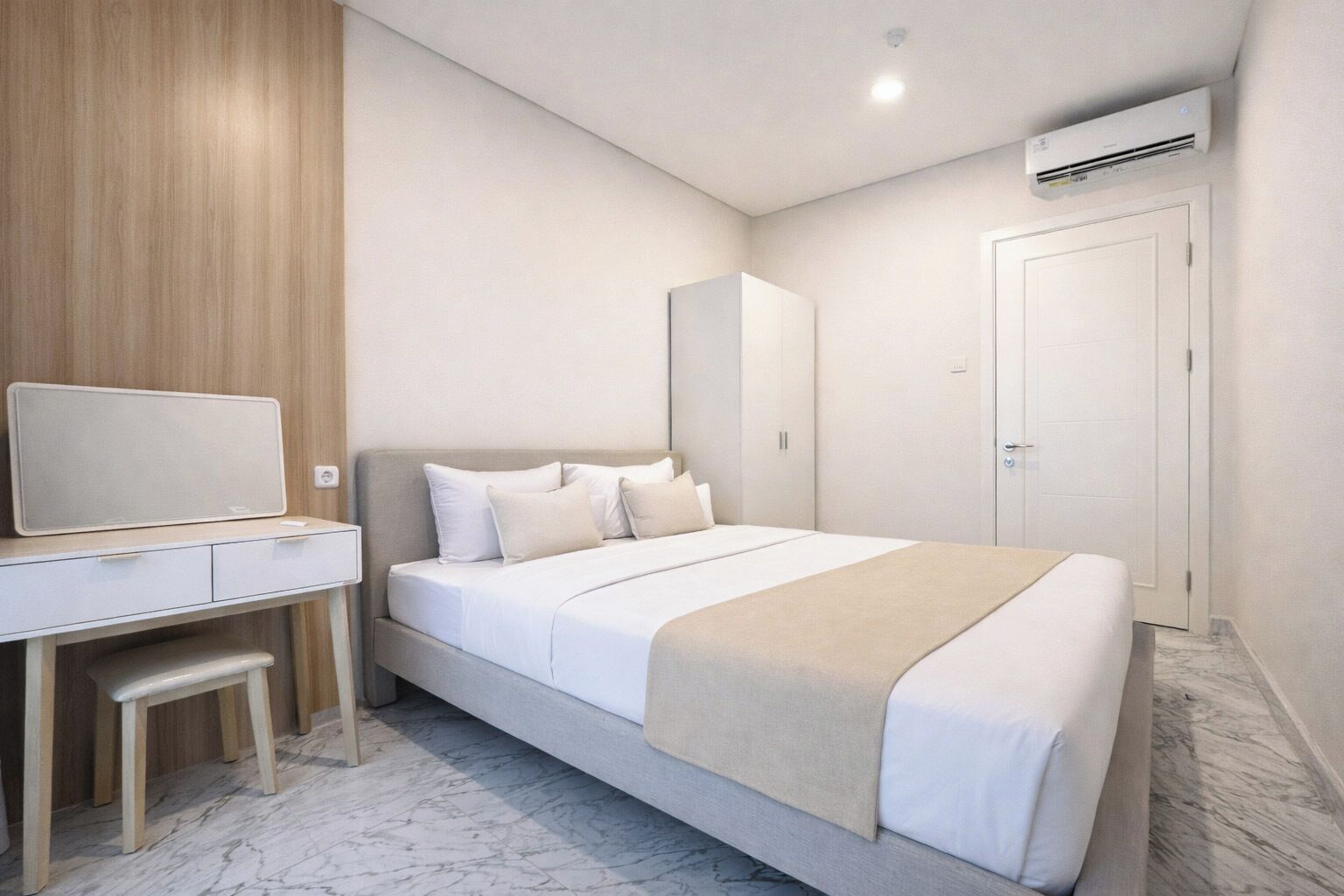 A hotel room with a bed, a desk with a chair, a wardrobe, and an air conditioning unit.
