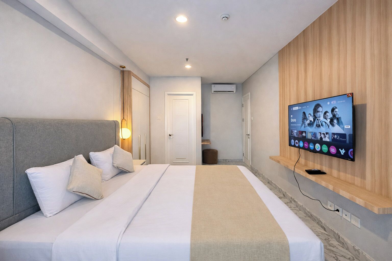 A hotel room with a bed, a TV mounted on the wall, and a door leading to another room.