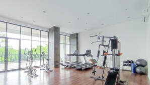 A spacious gym with cardio machines, weightlifting equipment, and a large window offering a view of greenery. - Lovely 1Br (No Living Room) At Apartment Cordova Edupartment Semarang (Semarang)