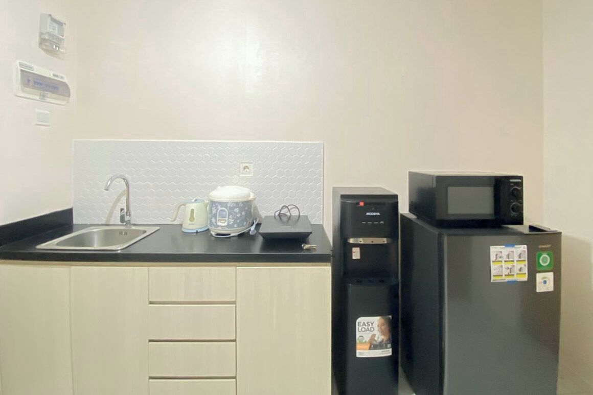 A kitchen with a sink, kettle, microwave, and refrigerator.