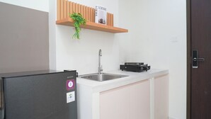 A kitchen with a refrigerator, a sink, a countertop, and a wooden shelf with a plant. - Comfortable And Decent Studio At Apartment Daan Mogot City (Jakarta)