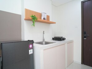 Eine Küche mit Kühlschrank, Spüle, Arbeitsplatte und einem Holzbodenregal mit einer Pflanze.