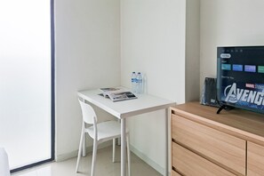 A modern room with a white desk, two water bottles, a magazine, and a TV displaying the Marvel Studios logo. - Functional And Strategic Studio At Apartment Daan Mogot City (Jakarta)