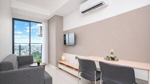 Et moderne hotelværelse med et stort vindue, et fladskærms-tv, et skrivebord med to stole og en sofa.