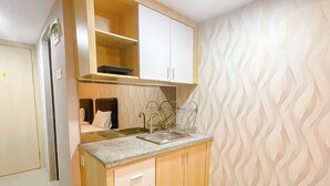A compact kitchen with wooden cabinets, a countertop, and a patterned wall. - Homely And Pleasant Studio At Apartment De Prima (Medan)