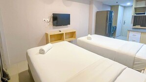 A hotel room with two beds, a television, a small wooden shelf, and a kitchenette. - Homely And Pleasant Studio At Apartment De Prima (Medan)