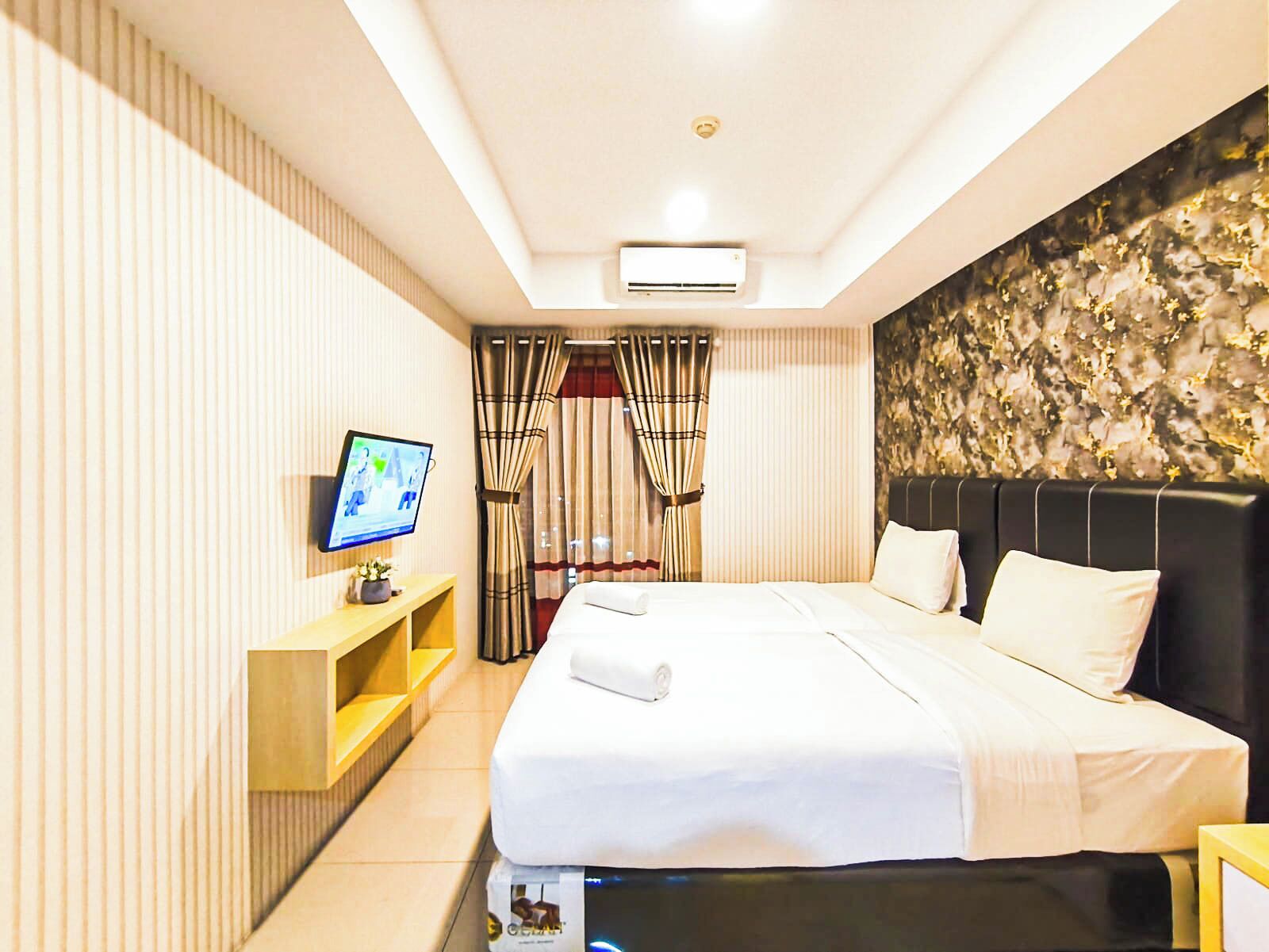 Quarto de hotel com cama, televisão, escrivaninha e ar condicionado fixado na parede.