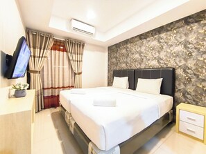 A hotel room with a bed, a TV, curtains, an air conditioner, and a wall with a textured pattern. - Neat Studio At De Prima Apartment (Medan)