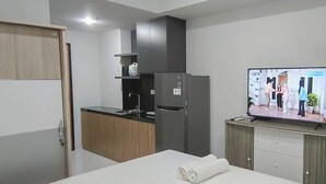 Habitación de hotel moderna con cama, televisión, kitchenette y armario de madera.