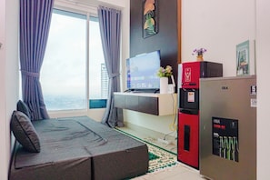Una sala moderna con un sofá, un televisor de pantalla plana, un refrigerador y vistas a la ciudad.