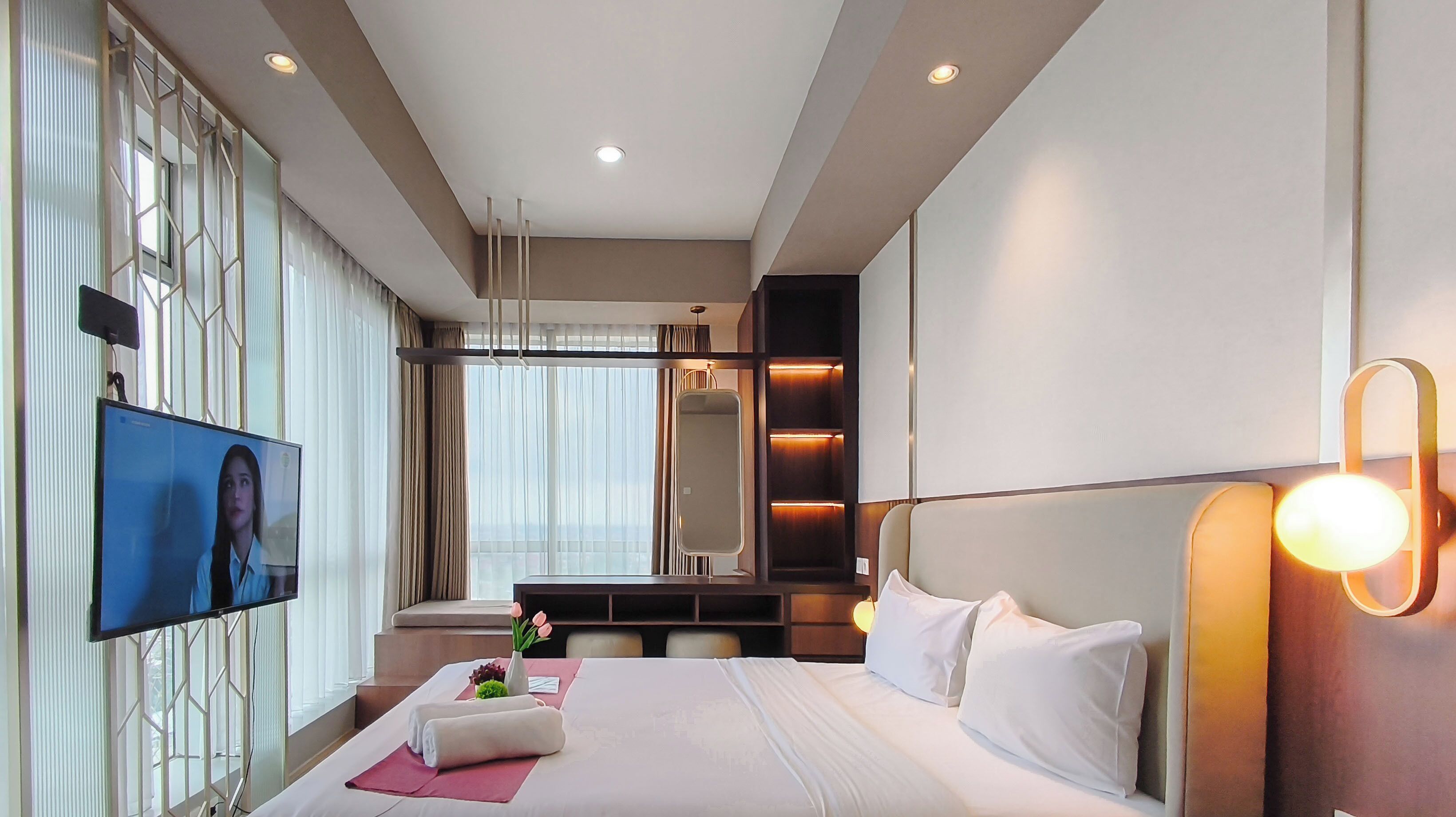A modern hotel room with a large bed, a television, a desk, and a large window.