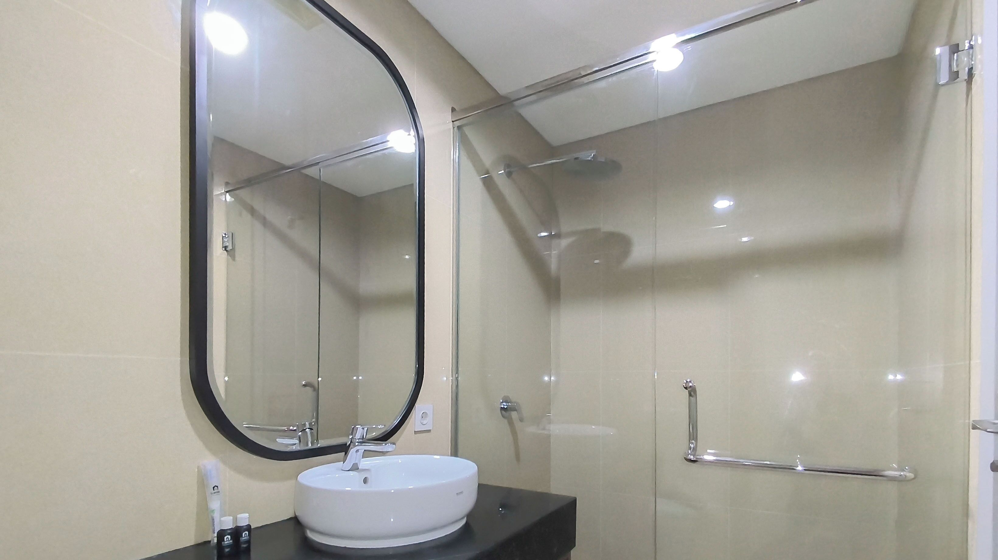 Une salle de bain moderne avec un miroir rond, un lavabo blanc et une douche à parois de verre.