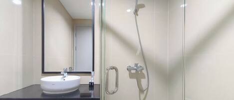 Un baño con ducha envuelta en vidrio, un lavabo blanco y un espejo.