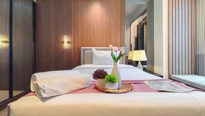 Ein Hotelzimmer mit einem ordentlich bezogenen Bett, einer Nachttischlampe, einer Vase mit Blumen und einer kleinen Pflanze auf dem Nachttisch.