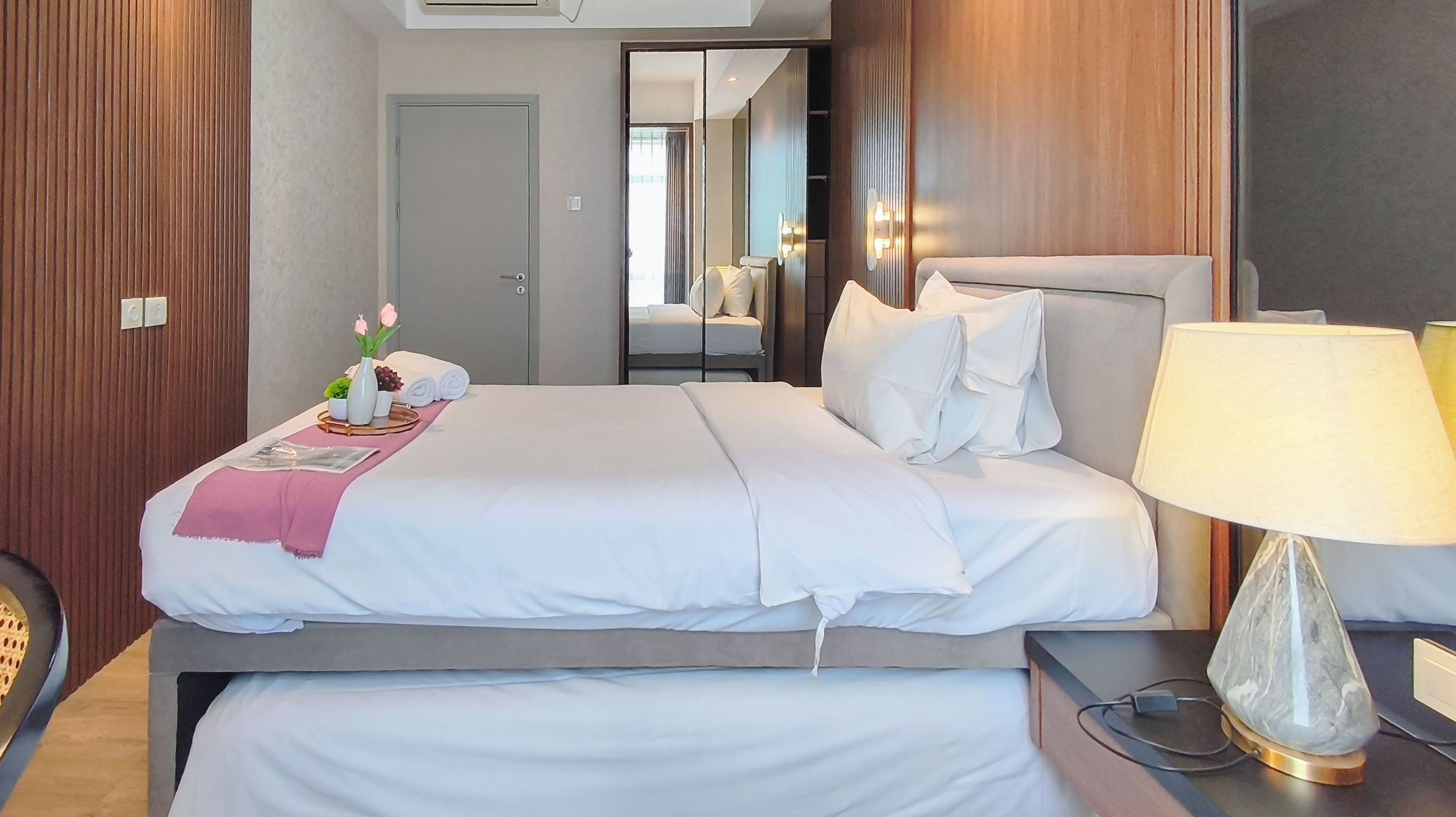 A hotel room with a bed, bedside table, lamp, and a mirror.