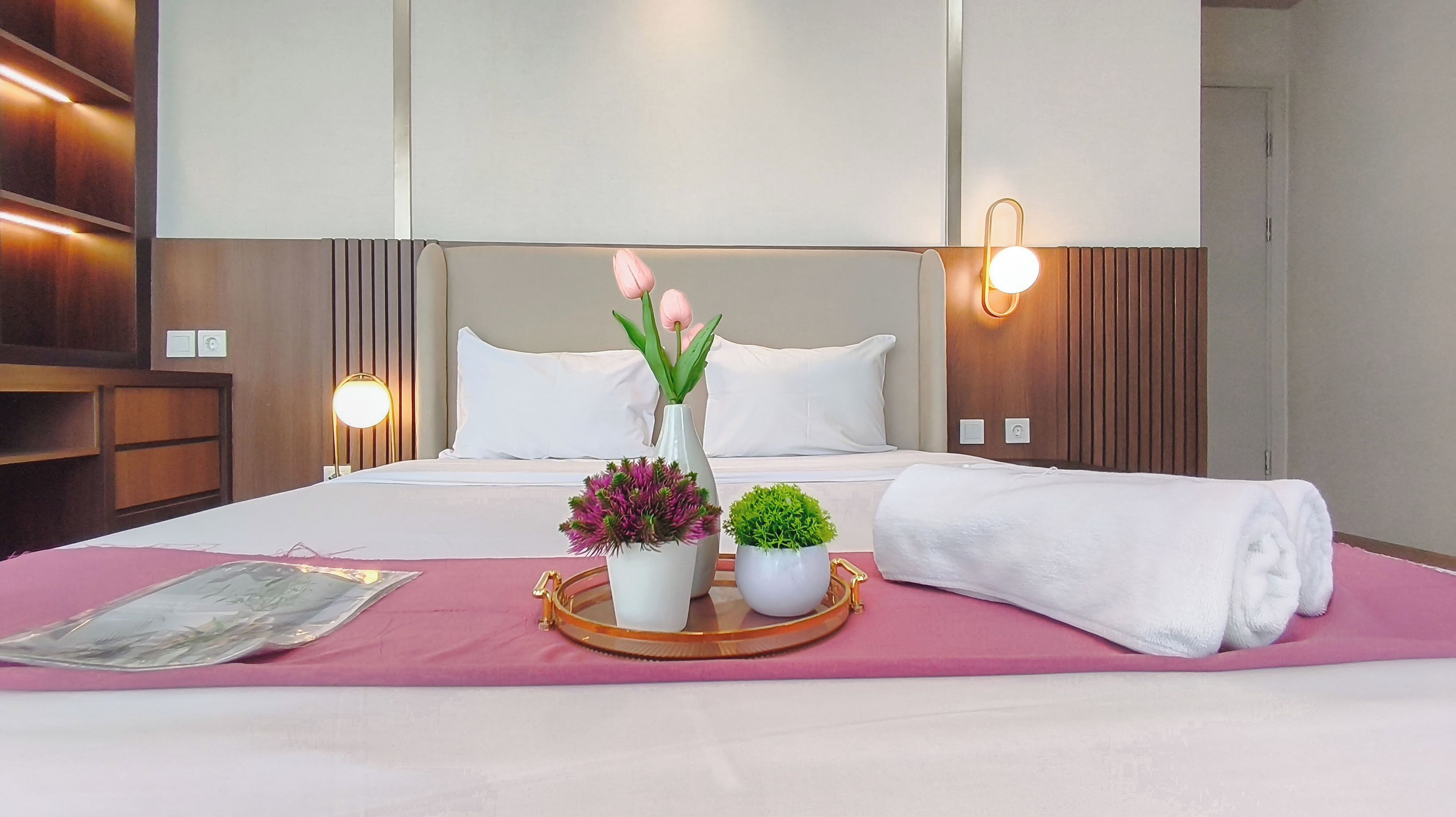 A hotel room with a bed, bedside lamps, a tray with plants, and a towel.