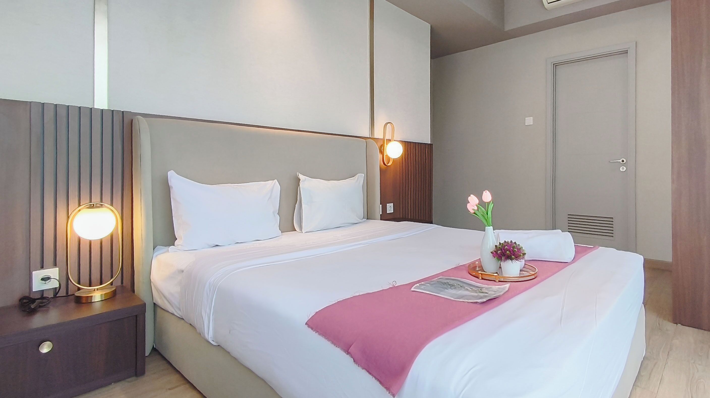A hotel room with a bed, bedside lamps, a nightstand, a door, and a wall-mounted light fixture.
