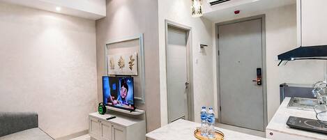 Una habitación de hotel moderna con televisión de pantalla plana, zona de comedor con encimera de mármol, dispensador de agua y aire acondicionado instalado en el techo.