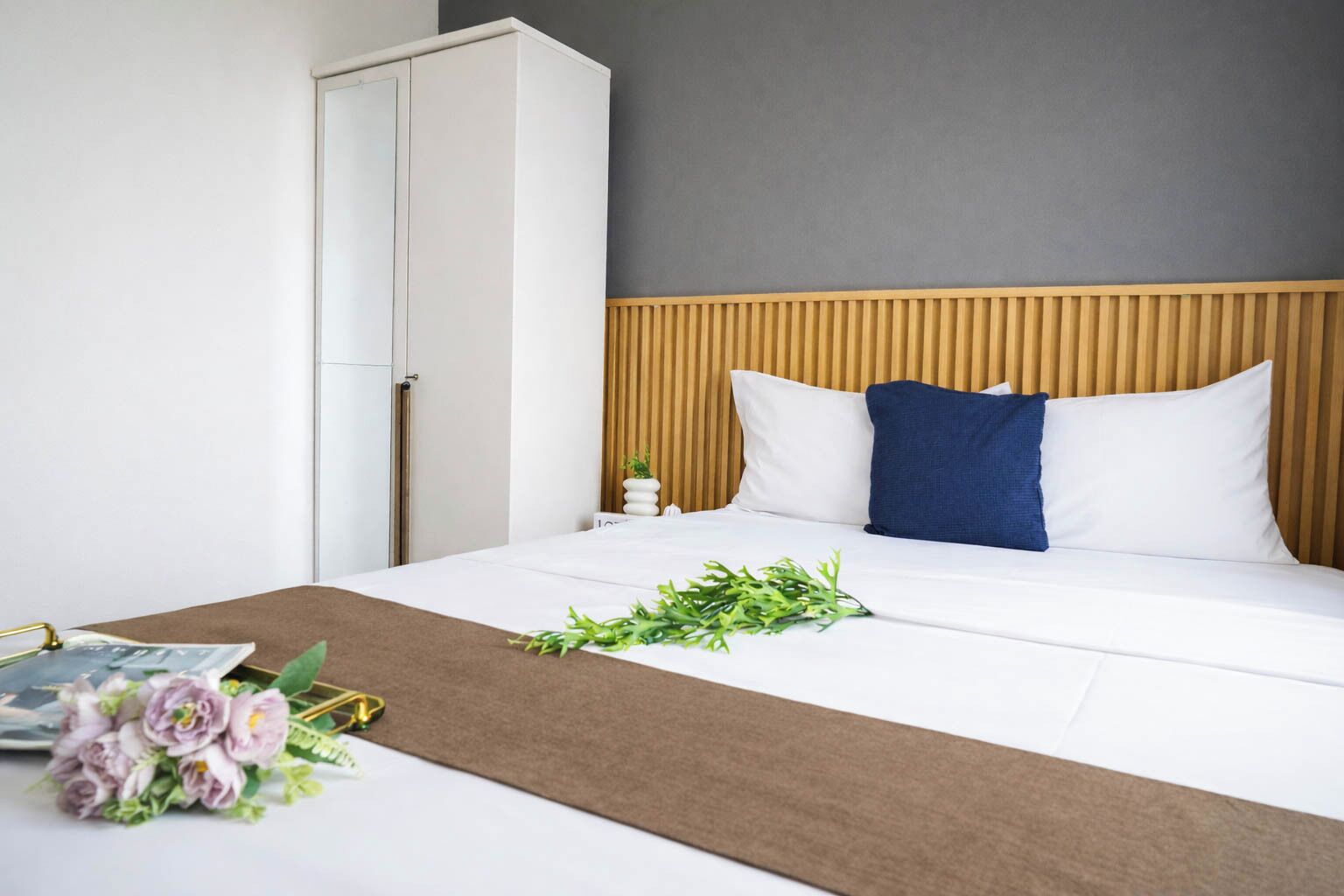 Habitación de hotel con cama, cabecero de madera, mesita de noche y armario.