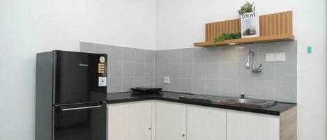 A kitchen with a black refrigerator, grey tiles, a wooden shelf with a plant, and a stainless steel sink.