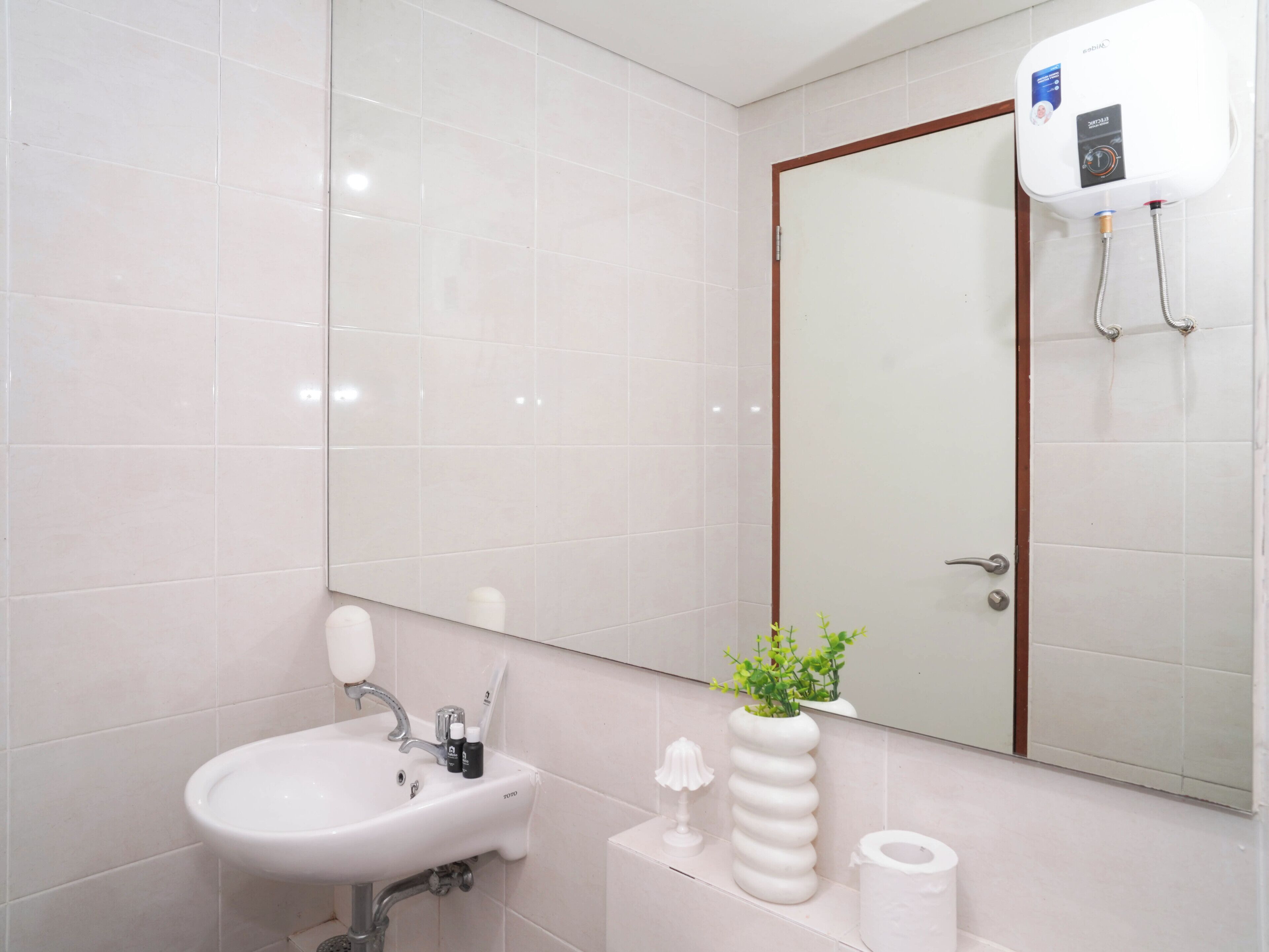 A bathroom with a white sink, mirror, toilet paper, and a water heater.