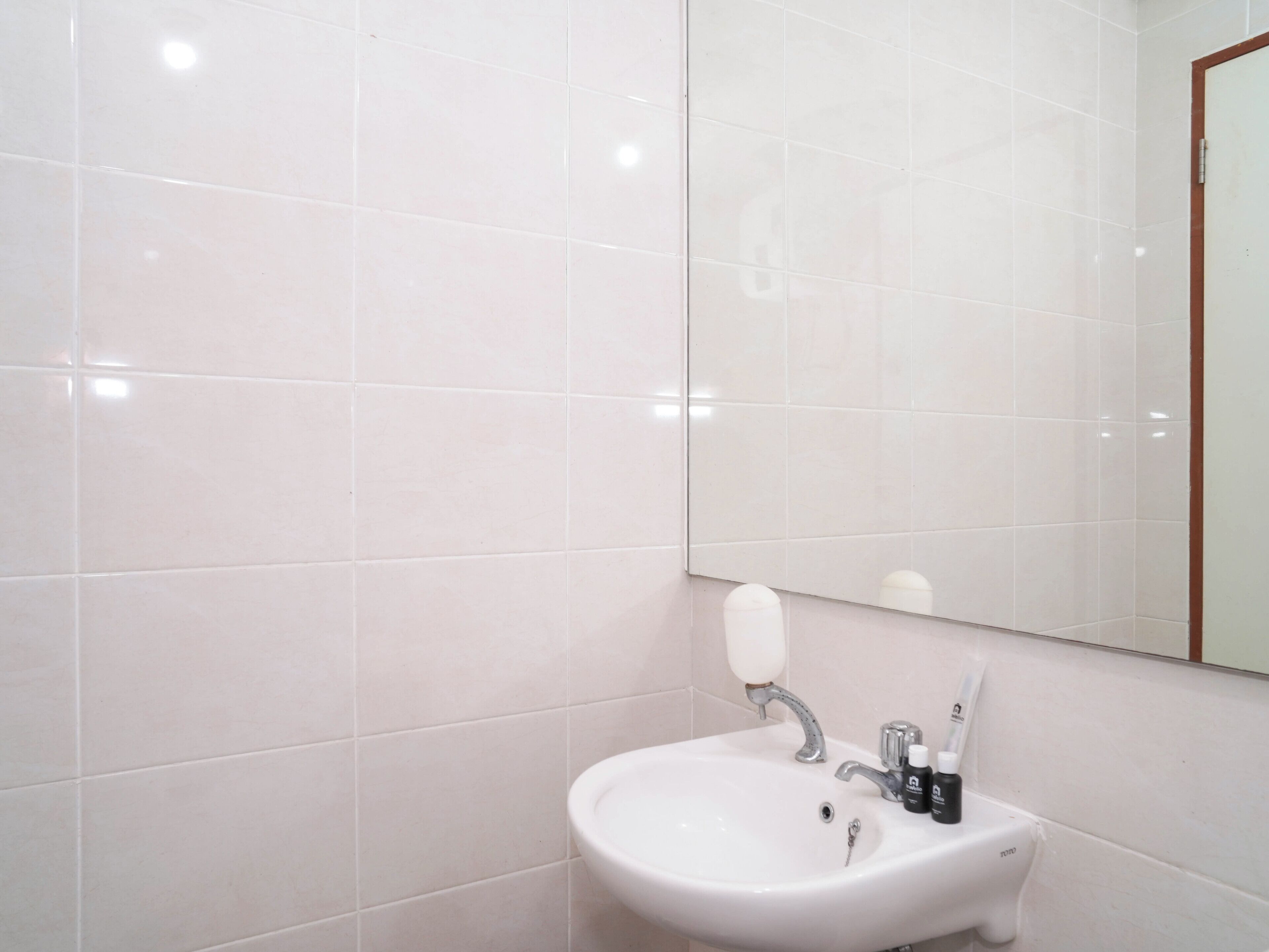 A bathroom with white tiles, a sink, a mirror, and a soap dispenser.