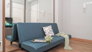 Una habitación con un sofá azul, un espejo, un televisor y un teléfono.