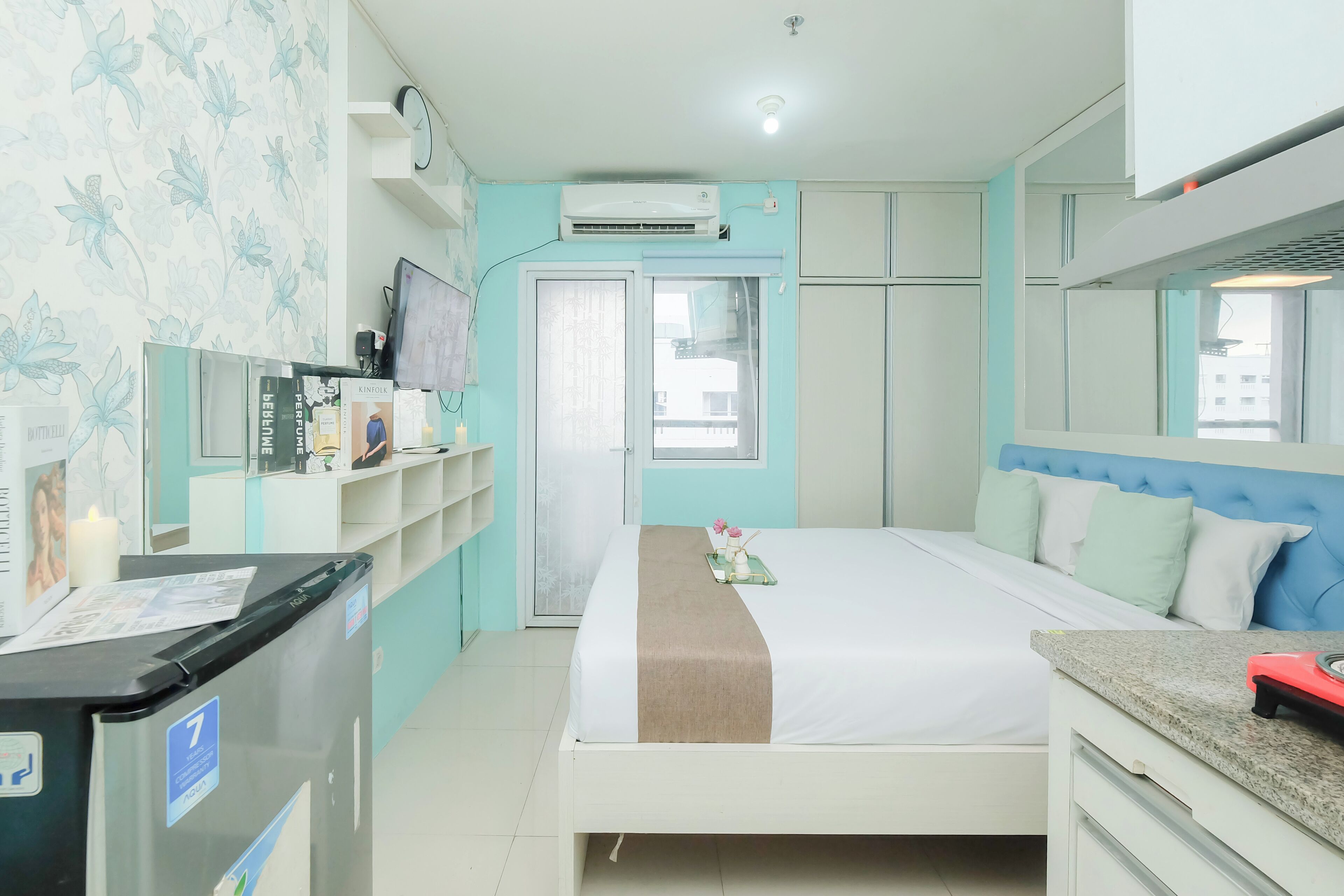 A hotel room with a bed, a desk, a wardrobe, and an air conditioning unit.