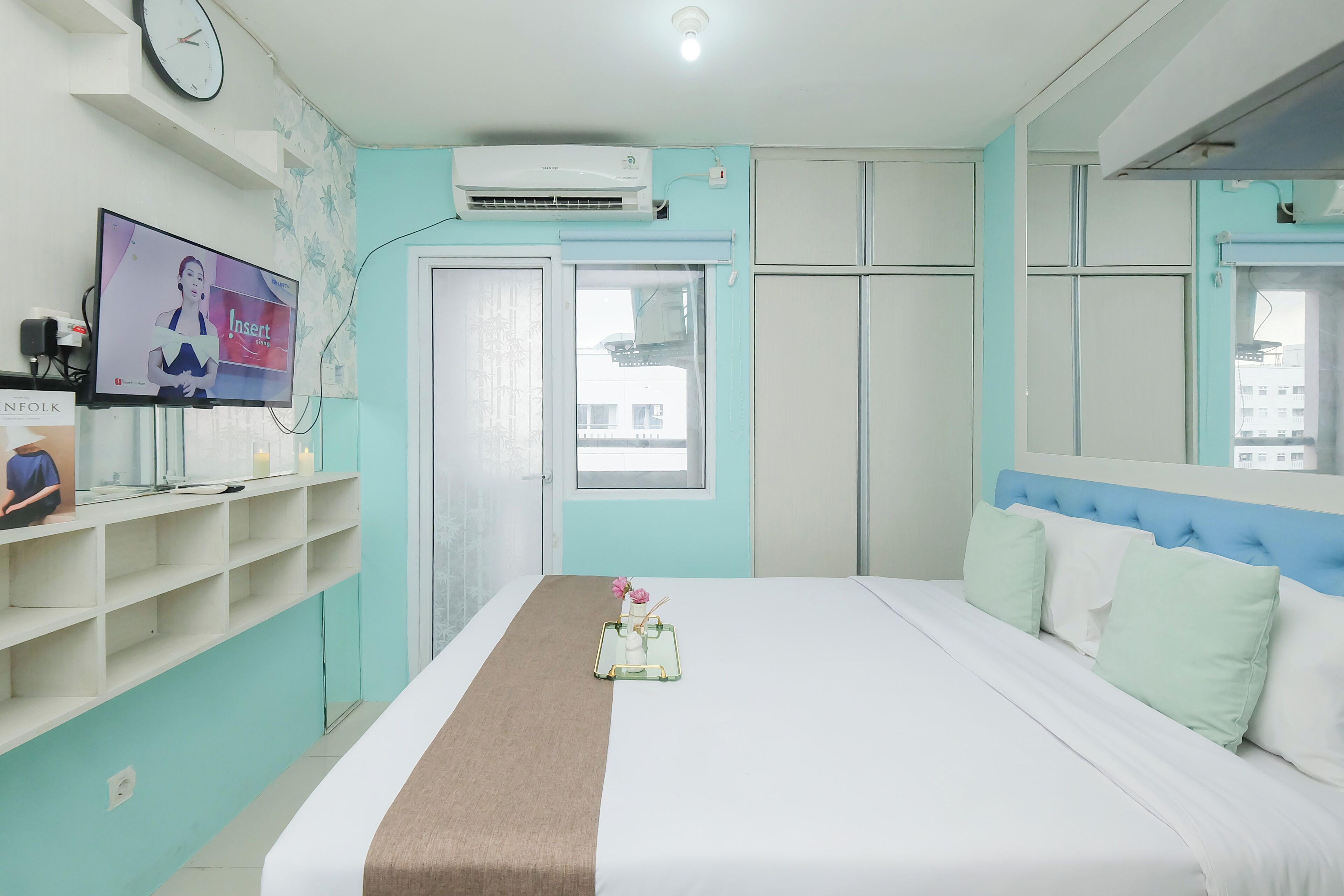 Une chambre d’hôtel avec un lit, une télévision, une étagère avec quelques objets et une fenêtre.