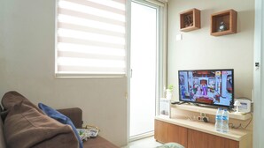 Olohuoneessa on sohva, televisio, puinen kaappi ja ikkuna, jossa on sälekaihtimet.