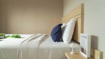 A neatly made bed with white linens, a blue pillow, and a small bedside table with a book titled 'LOEWE'.