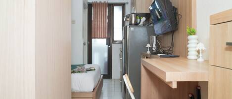 Een kleine hotelkamer met een bed, bureau, televisie, koelkast en een raam met gordijnen.