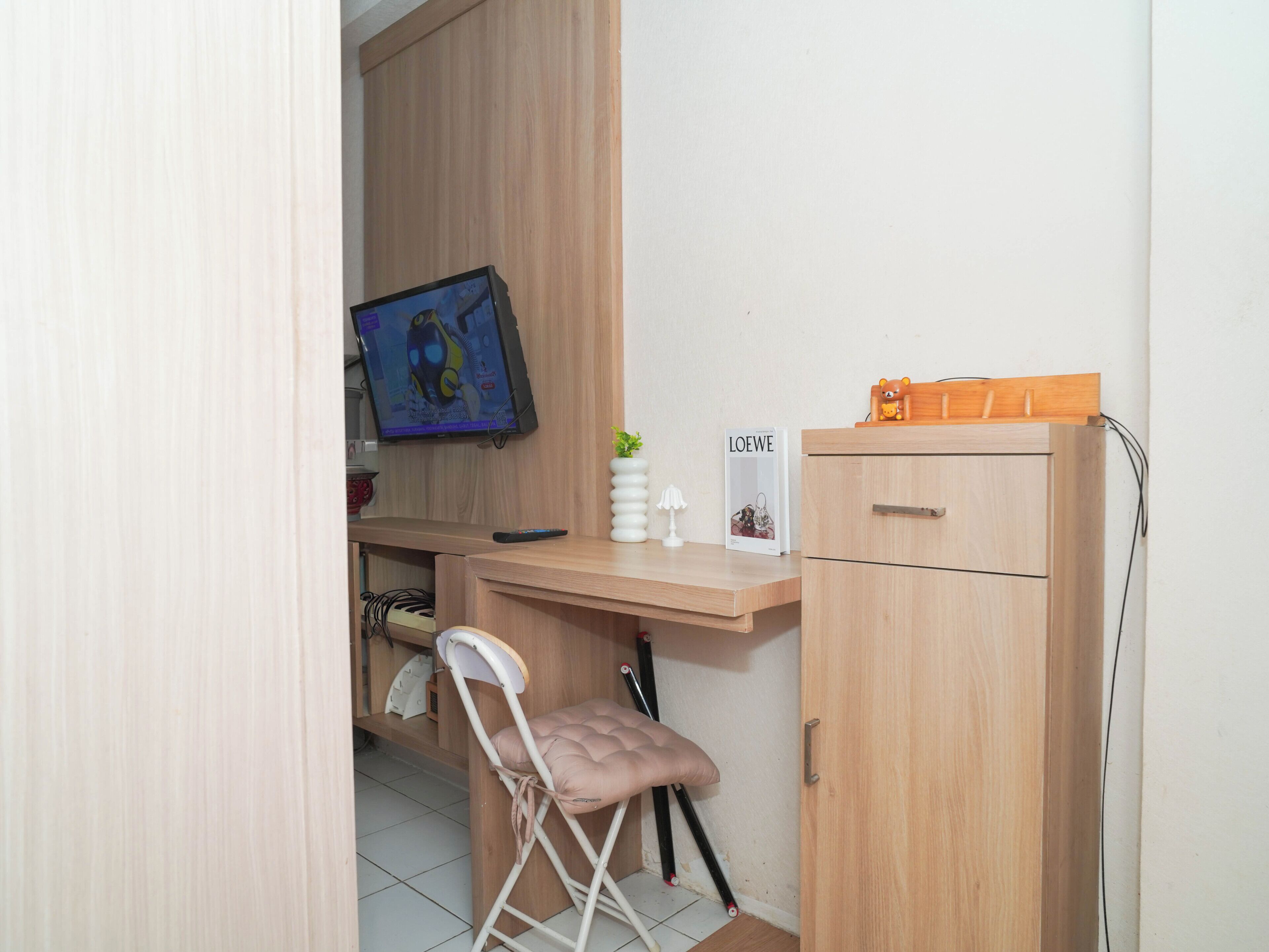 A small, neatly organized room with a wooden desk, a chair, a television, and a cabinet.